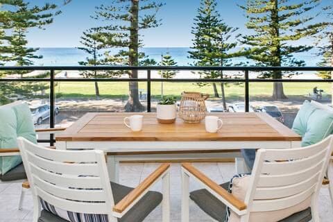 Balcony with an outdoor table looking over the Norfolk pines to Manly Beach